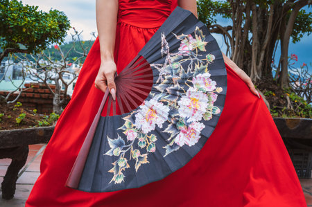 Beautiful Asian fan with flowers in a female hand in red dressの写真素材