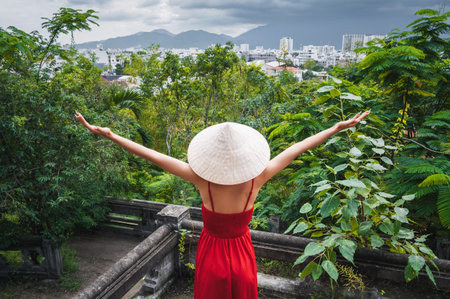 back of happy girl tourist traveler in Vietnamese non la hat in red dress in garden in Vietnam. Tourism and travel in Asiaの写真素材