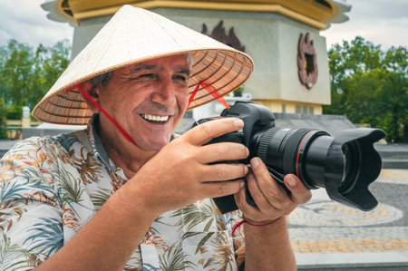 happy tourist adult man travel photographer in a Vietnamese hat takes pictures with camera at pagoda in Nha Trang in Vietnam. Tourism and travel in Asiaの写真素材