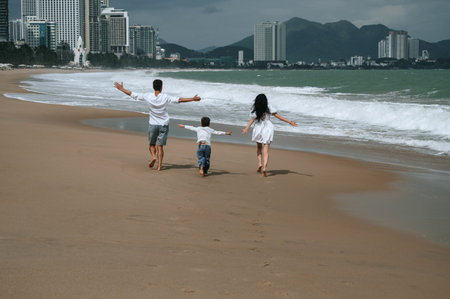 back of happy family with a child boy son running along the beach by sea in summer