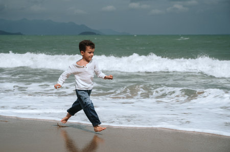 happy child boy running along beach by sea in summer on vacationの写真素材