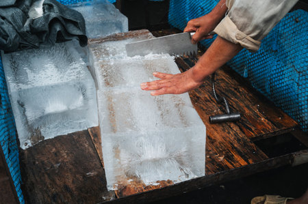 man cuts a block of ice for freezing and cocktails with a saw on the street in Asiaの写真素材