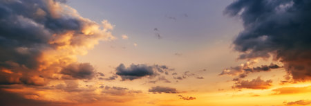 background with an orange sunset on a cloudy sky with blue clouds. Wide panorama of sky at sunriseの写真素材