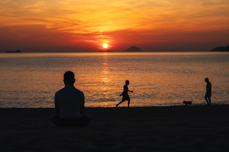 Silhouettes of people relaxing on beach by the sea in the evening at sunset in summer on vacationの写真素材