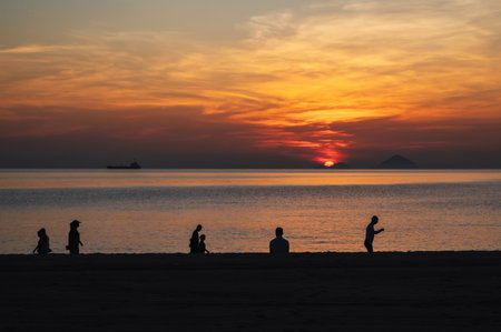 Silhouettes of people relaxing on beach by the sea in the morning at sunrise in summer on vacationの写真素材