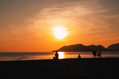 silhouette of a man sitting and meditating on the beach by the sea in evening at sunset in summerの写真素材
