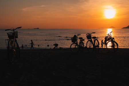 Silhouettes of people and bicycles on beach by the sea in the morning at sunrise in summer on vacationの写真素材