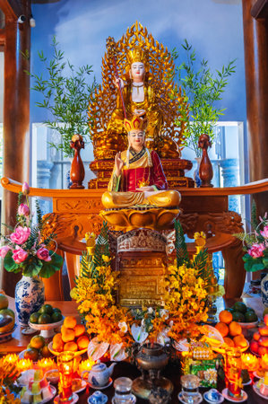golden Buddha on an altar decorated with fresh flowers inside a Buddhist templeの写真素材
