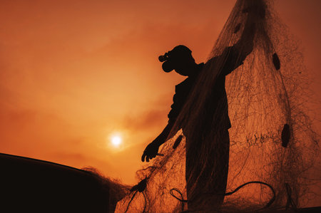 Silhouette of a Vietnamese male fisherman taking out a catch of fish from fishing net in boat on beach by the sea in a fishing village in the morning at sunrise in Vietnamの写真素材
