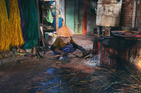 Vietnamese woman wearing a traditional straw hat works in a cane dyeing workshop at a woven mat factory in Vietnam.の写真素材