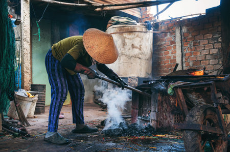 Vietnamese female stoker worker works in a workshop and lights a coal furnace at reed dyeing plant...