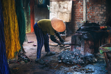 Vietnamese woman in traditional straw hat works in reed dyeing workshop at a woven mat factory in Vietnam.の写真素材
