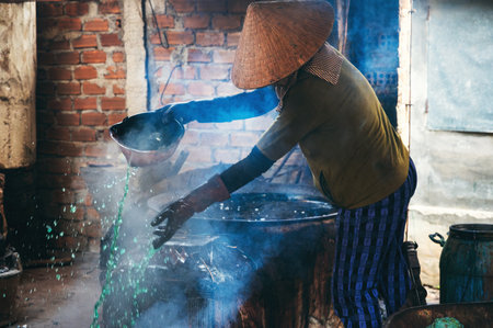 Vietnamese female worker puts out a fire in furnace in workshop at a factory in village. Asian woman does dirty hard work in a factory in Asiaの写真素材