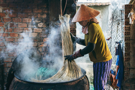 Vietnamese woman in a traditional straw hat dyes reeds at a woven mat factory in Vietnamの写真素材