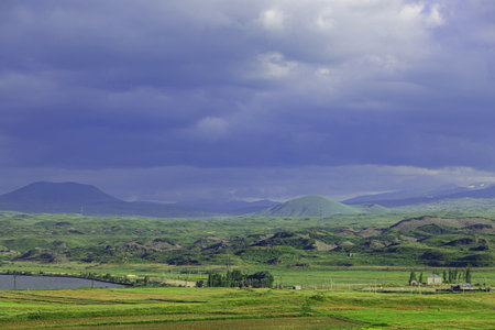 Brooding clouds loom over the lush fields and rolling hills at dusk in Armenia.