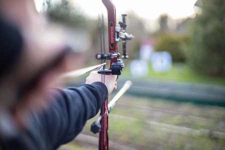 A close-up view of an individual holding a bow and arrow, showcasing a concentrated expression as...