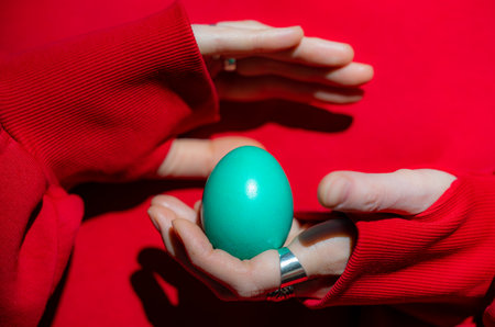 A person delicately holds a colorful Easter egg in their hands, showcasing the fragility and beauty of the holiday symbol.の写真素材