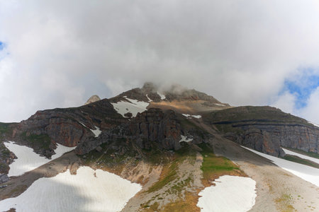 A low-angle shot capturing a mountain peak shrouded in mist, revealing patches of snow and rugged...