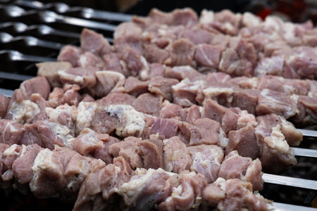 A close-up of raw meat cubes, marinated and skewered, ready to be cooked on a hot grill.の写真素材