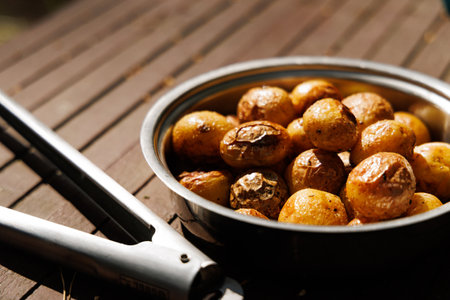 A bowl of freshly roasted potatoes sits on a wooden table, glistening with oil and ready to be eaten.の写真素材