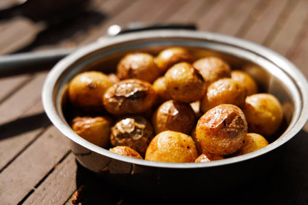 A bowl filled with freshly roasted potatoes sits on a wooden table, bathed in warm sunlight.の写真素材