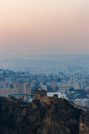 Snow blankets the hills as Tbilisi glimmers under a soft winter sunset, blending history with serene...