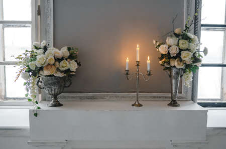 Metal candle holder with burning candles and vases with artificial flowers on a pedestal.の写真素材