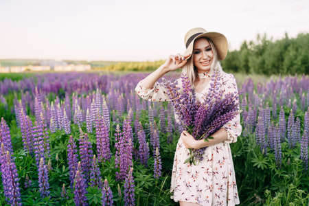 a blonde girl in a dress straw hat holding a bouquet of lupins.の写真素材