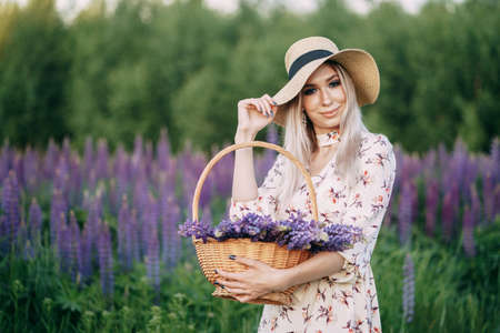 blonde girl in a dress with a basket in a field of lupins.の写真素材