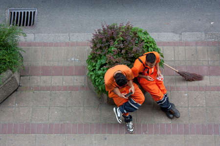 Street cleaners on a break, smoking cigarette and using mobile, a broom next to them, shot from above.のeditorial素材
