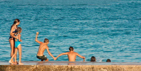 Vodice, Croatia - August 21, 2016: Two young girls watching four pre-adolescent boys holding hands while jumping into the sea from the pier.のeditorial素材