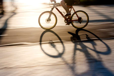 Blurry cyclist silhouette and shadow on a  bike path  in sunset, panning shot