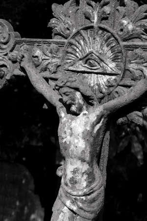 Small casted metal  statue of crucified Jesus Christ with an Eye of Providence ( all seeing eye of God ) at the old cemetery in Serbia, detail in black and whiteの写真素材