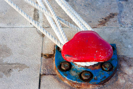 Retro rusty red and blue dock bollard on the stone pier with ropes for the fastened shipの写真素材