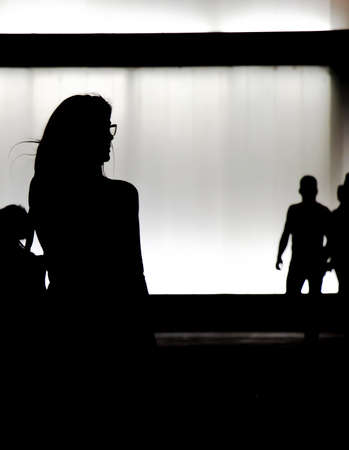 Silhouette of a young woman walking alone in the night and a group of people approachingの写真素材