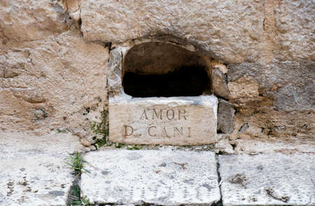 Watering hole , stone made bowl in the facade wall of house in old town Sibenik main street, with latin sign AMOR D CANI , was man-made to provide drinking water for dogs ( and cats ) and is regularly filled with fresh waterの写真素材