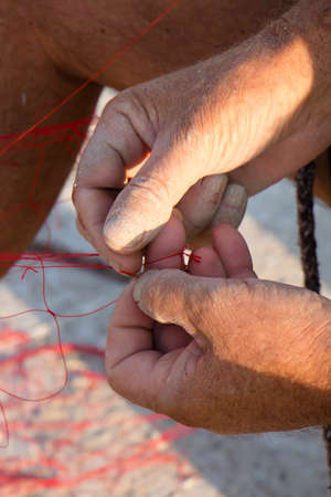 Fisherman hands repairing his red fishing net , close up detail