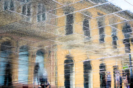 Blurry reflection shadow silhouette in a puddle of people walking on rainy city streetの写真素材