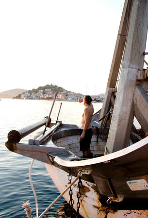 Tribunj, Croatia - August, 24, 2018: Fisherman standing on a front deck of a moored trawler boat and looking at distanceのeditorial素材