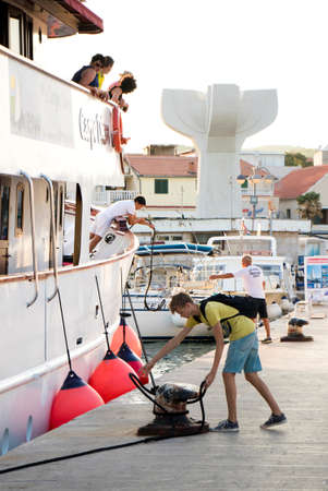 Vodice, Croatia - August 11, 2018: A cruise ship Carpe Diem arriving in Vodice and  docking. A man and a teenage boy on a pier fastening the ship ropes on a bollard while  passengers watchingのeditorial素材
