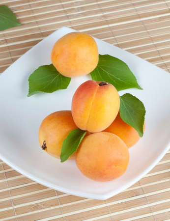 Yellow ripe apricot with green leaves on a plateの写真素材