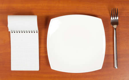 Background with  plate with  fork and  notebook on  wooden boardの写真素材