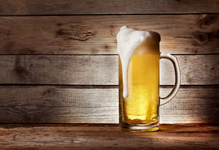 Mug of light beer with foam on wooden tableの写真素材