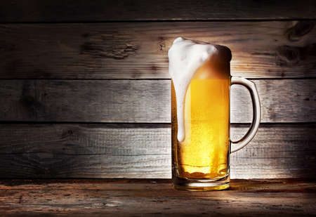 Mug of light beer with foam on wooden tableの写真素材