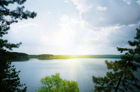Blue lake between the trees under cloudy sky