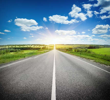 Asphalt road in field under blue cloudy skyの写真素材