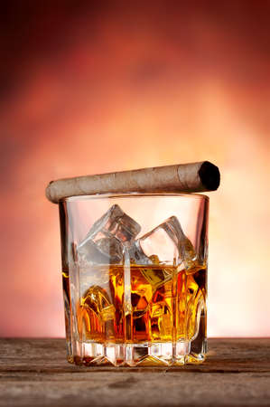 Faceted glass with whiskey and cigar on a red backgroundの写真素材