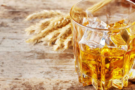 Faceted glass of whiskey with ice and ears on wooden tableの写真素材