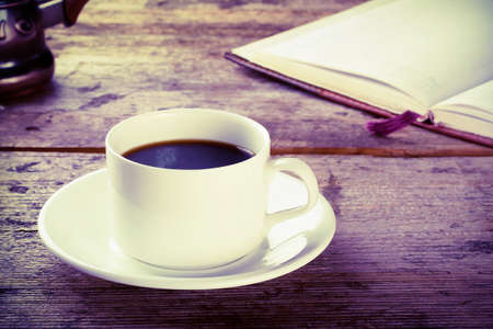 Cup of black coffee with a book on a wooden tableの写真素材