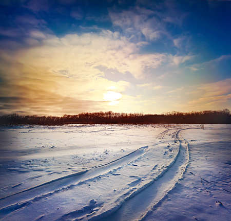 Road through snowy field under dramatic sunset skyの写真素材